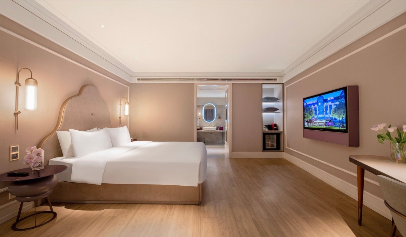 Hotel room with a bed beside floor-to-ceiling windows overlooking the Chengdu skyline at dusk.